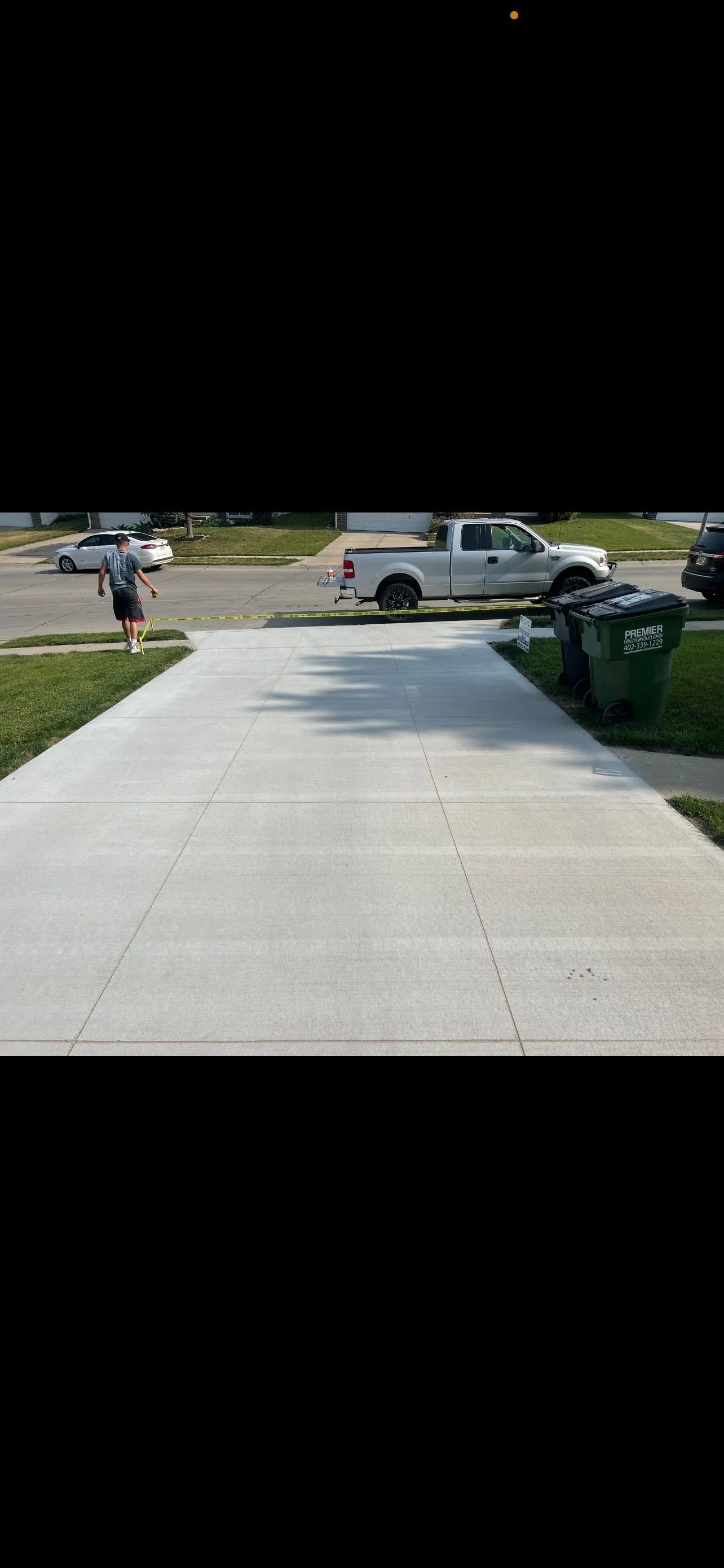 A person on a sidewalk near a white truck, trash bins, and a street.