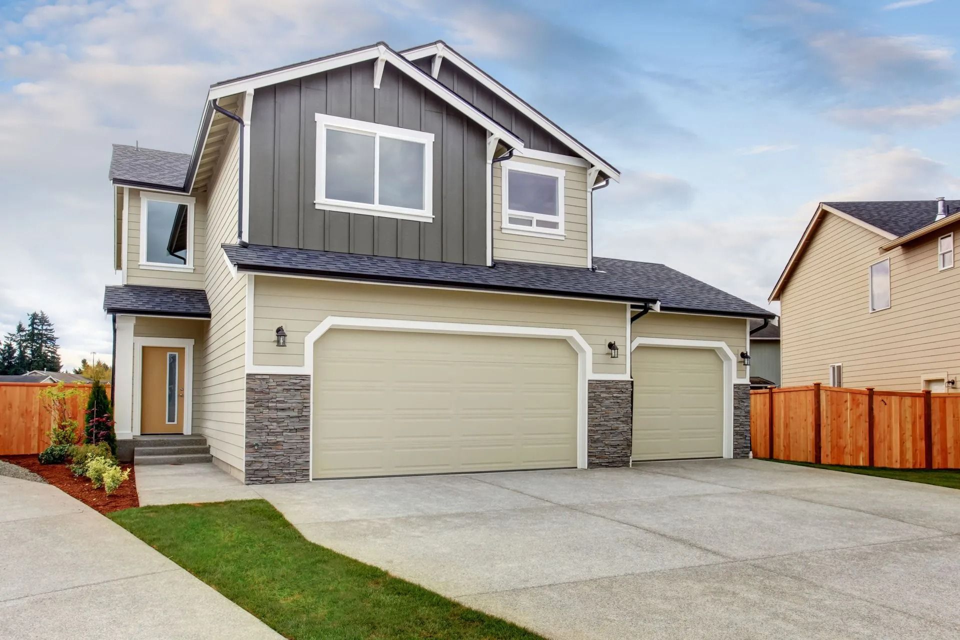 Two-story beige house with gray accents, two-car garage, and driveway under a blue sky.