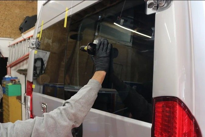 Worker polishing a white van window with a cloth in a garage-like workshop