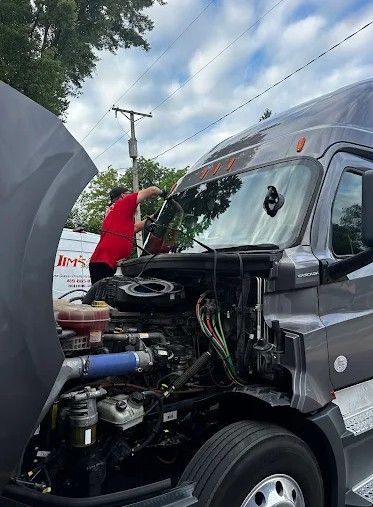 Person in red shirt inspecting a truck with its hood open on a roadside.