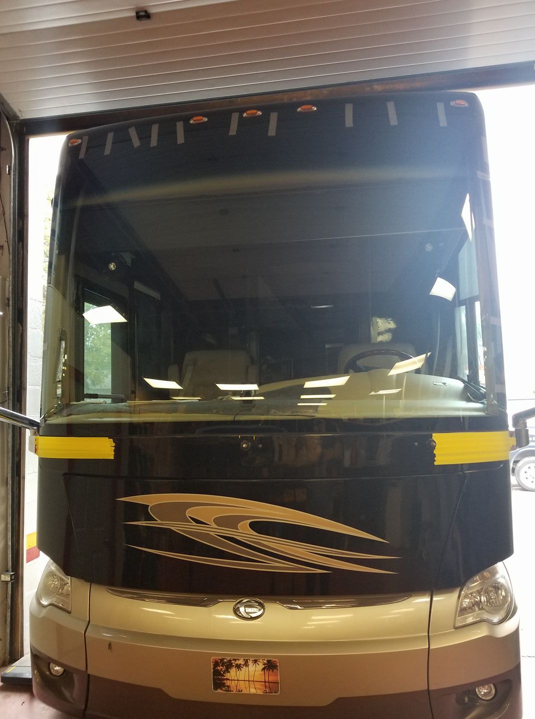 Front view of a black and beige bus parked indoors, with wide windshield and yellow side accents