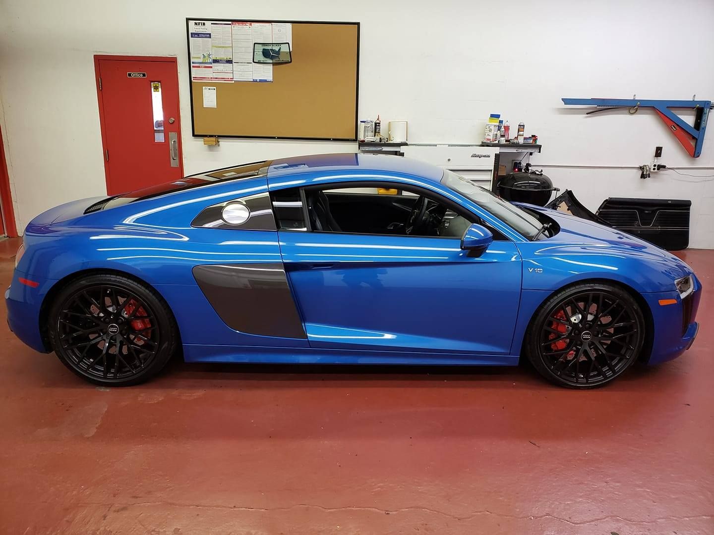 Blue sports car in a garage with black wheels and a red door in the background