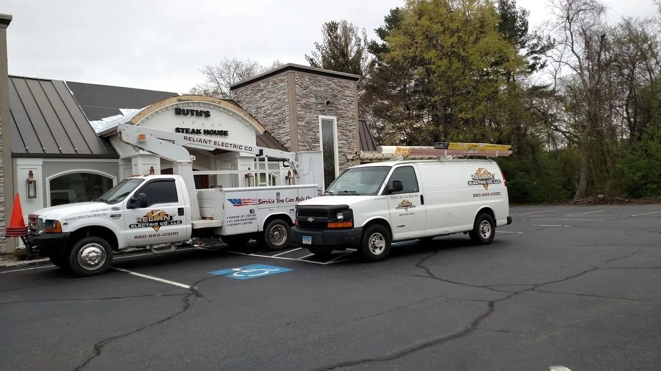 Two work trucks parked in front of a building. One has a crane, both have logos.