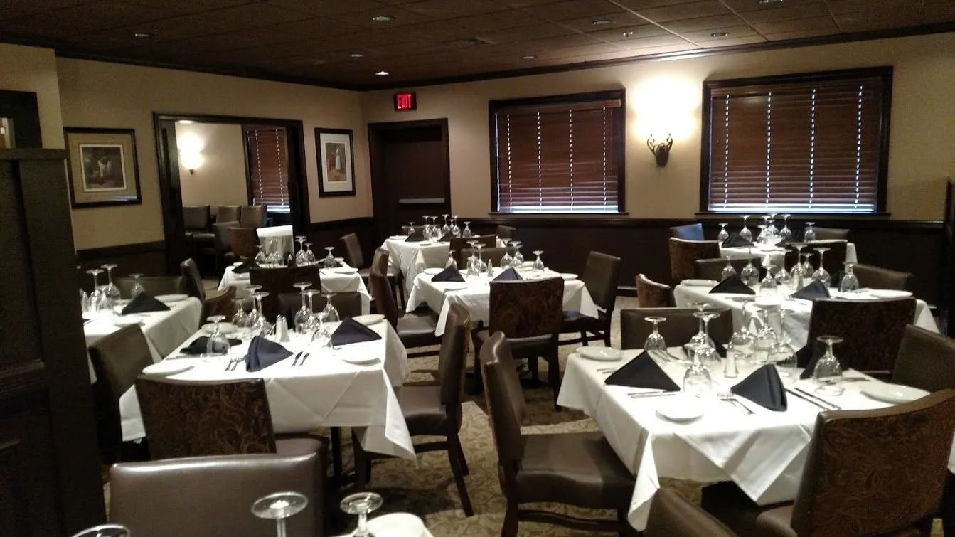 Formal dining room with white tablecloths, dark chairs, and place settings.