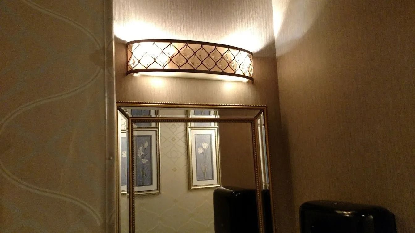 Mirror with ornate gold frame, lit by wall-mounted light. Two framed pictures reflected in the mirror.