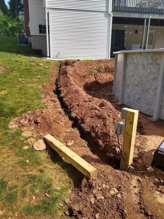A trench dug in a backyard, leading towards a pool and house with white siding.