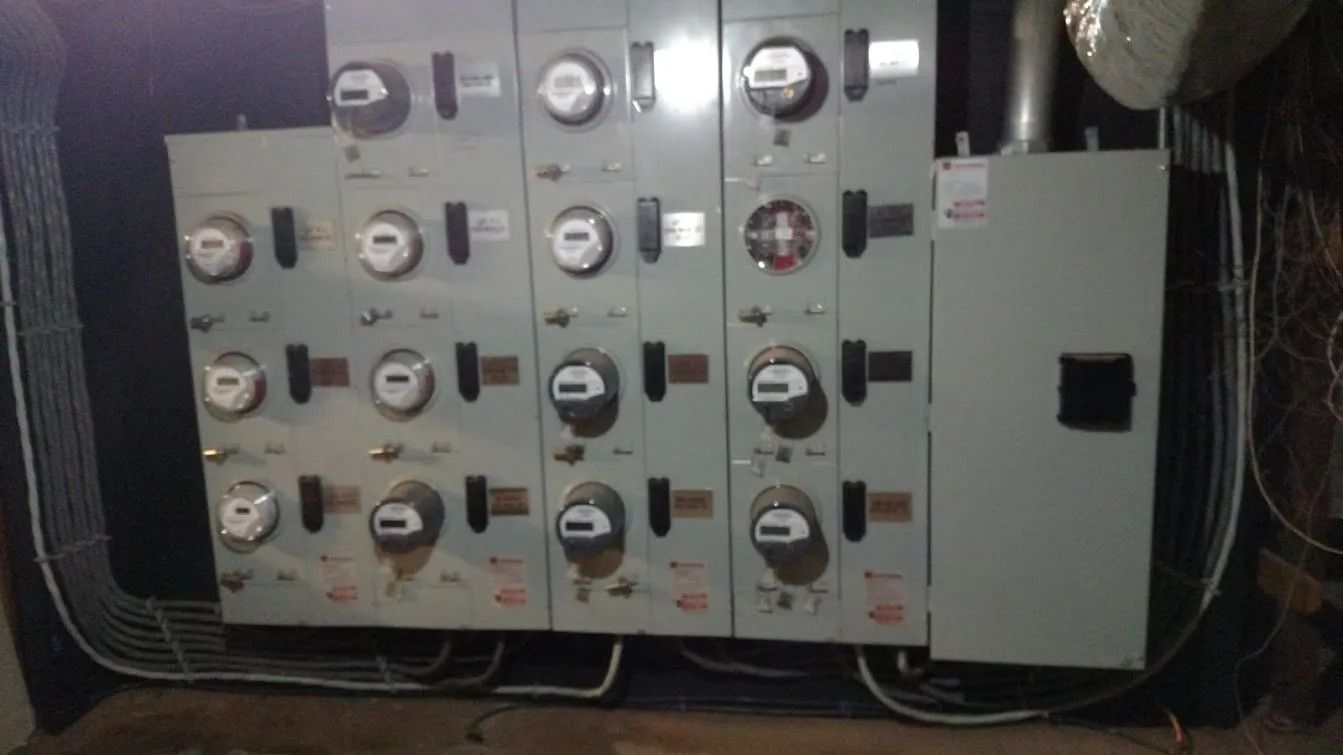Electrical meters on a gray panel in a basement. Wires run along the floor.