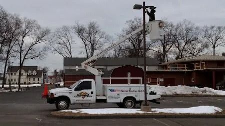 A utility truck with an extended boom lifts a person working on a lamppost on a cloudy day.