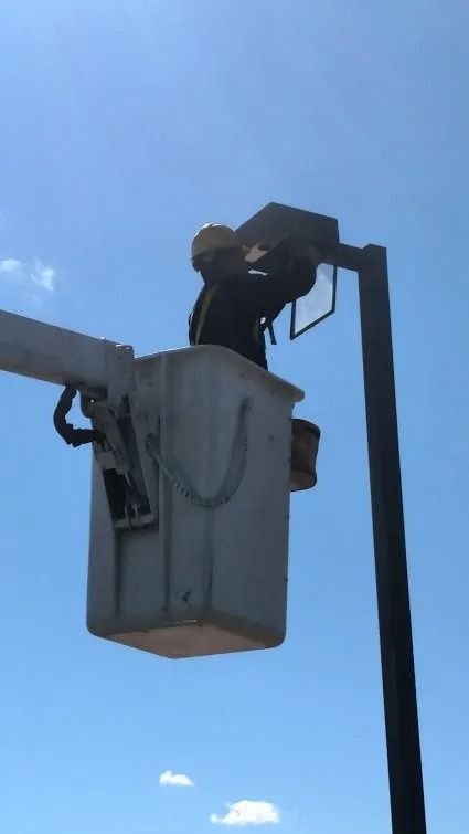 Worker in a bucket lift repairing a street light against a clear blue sky.