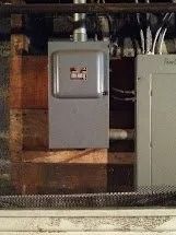 Electrical panel and meter box mounted on wooden boards, wiring visible.