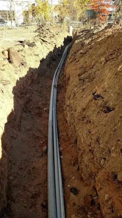 Trench with multiple gray pipes, likely for utilities, running through brown dirt.