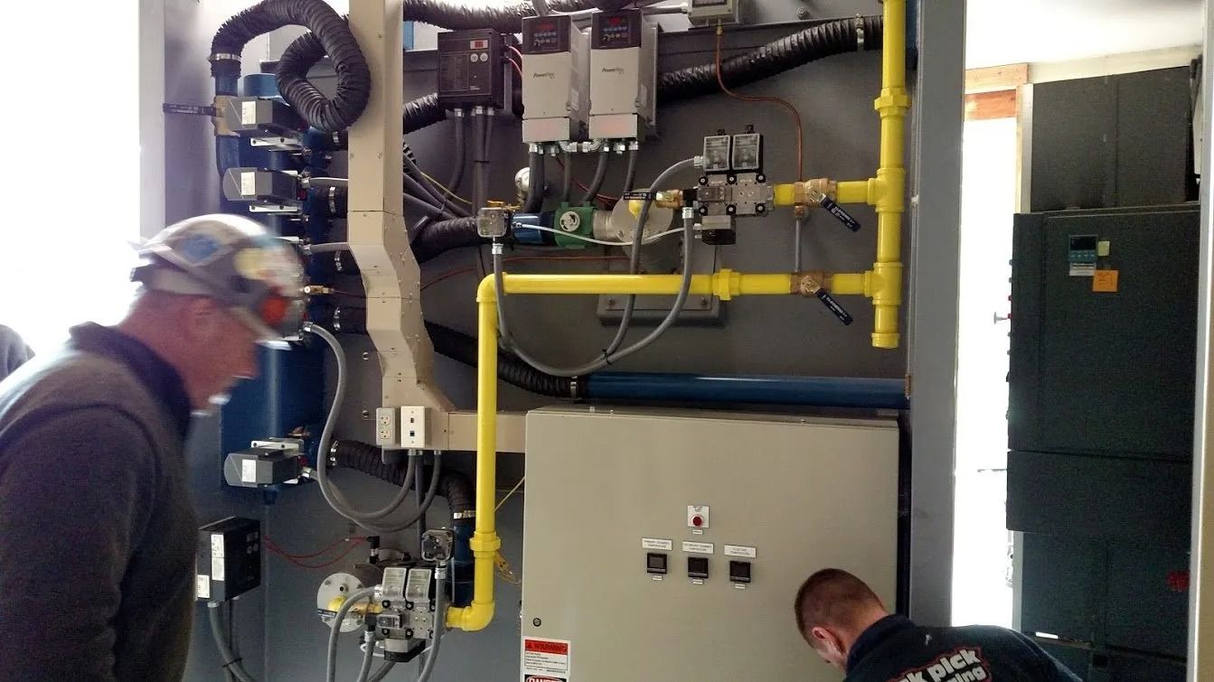 Two men inspecting industrial equipment with yellow gas pipes and control panels.