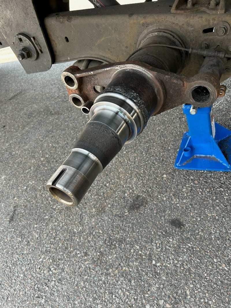 Car wheel hub and axle spindle on a car, supported by a blue jack stand in a garage.
