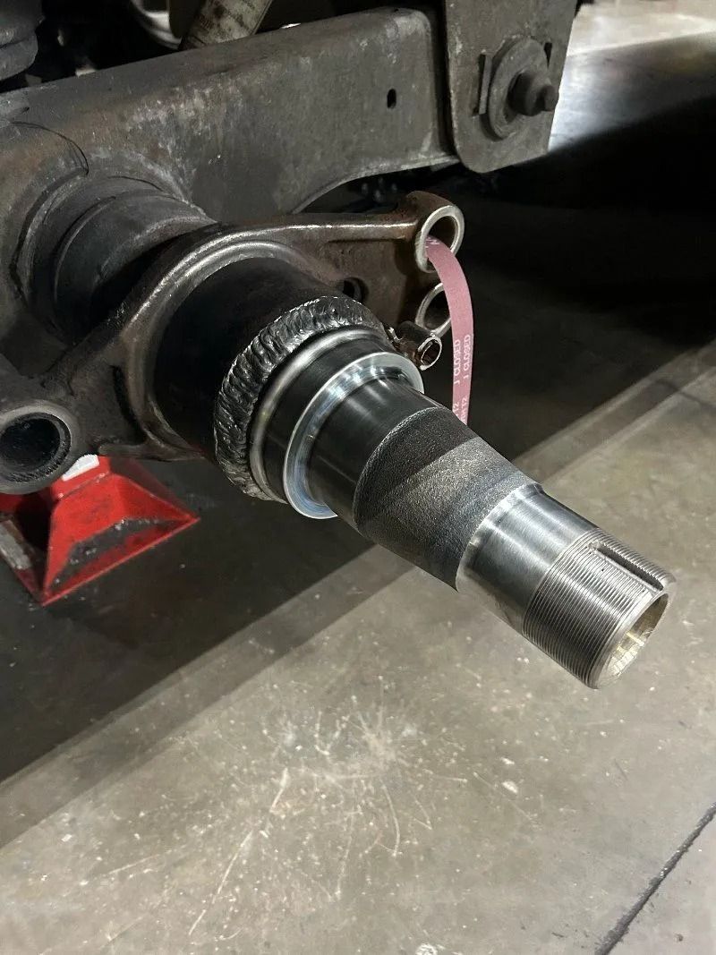 Close-up of a metal axle shaft protruding from a machine, with a threaded end and grease on the surface.