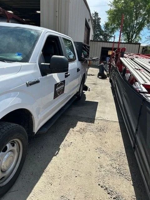 White utility truck parked in a narrow alley beside a building and dumpster, with a worker in the background