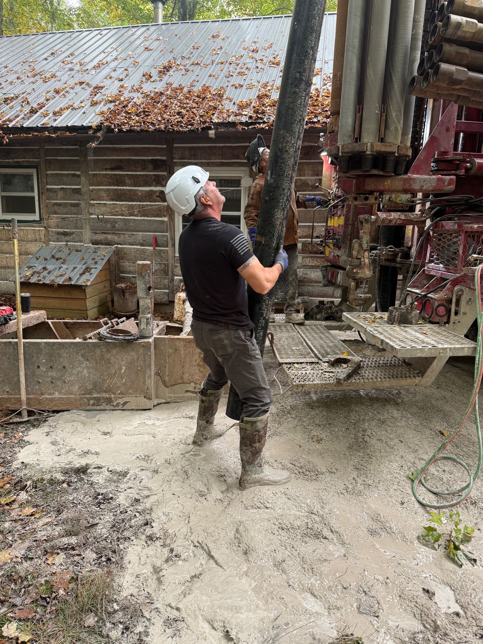 Worker in white hard hat operating a concrete pump beside a house with wet concrete splashing around him