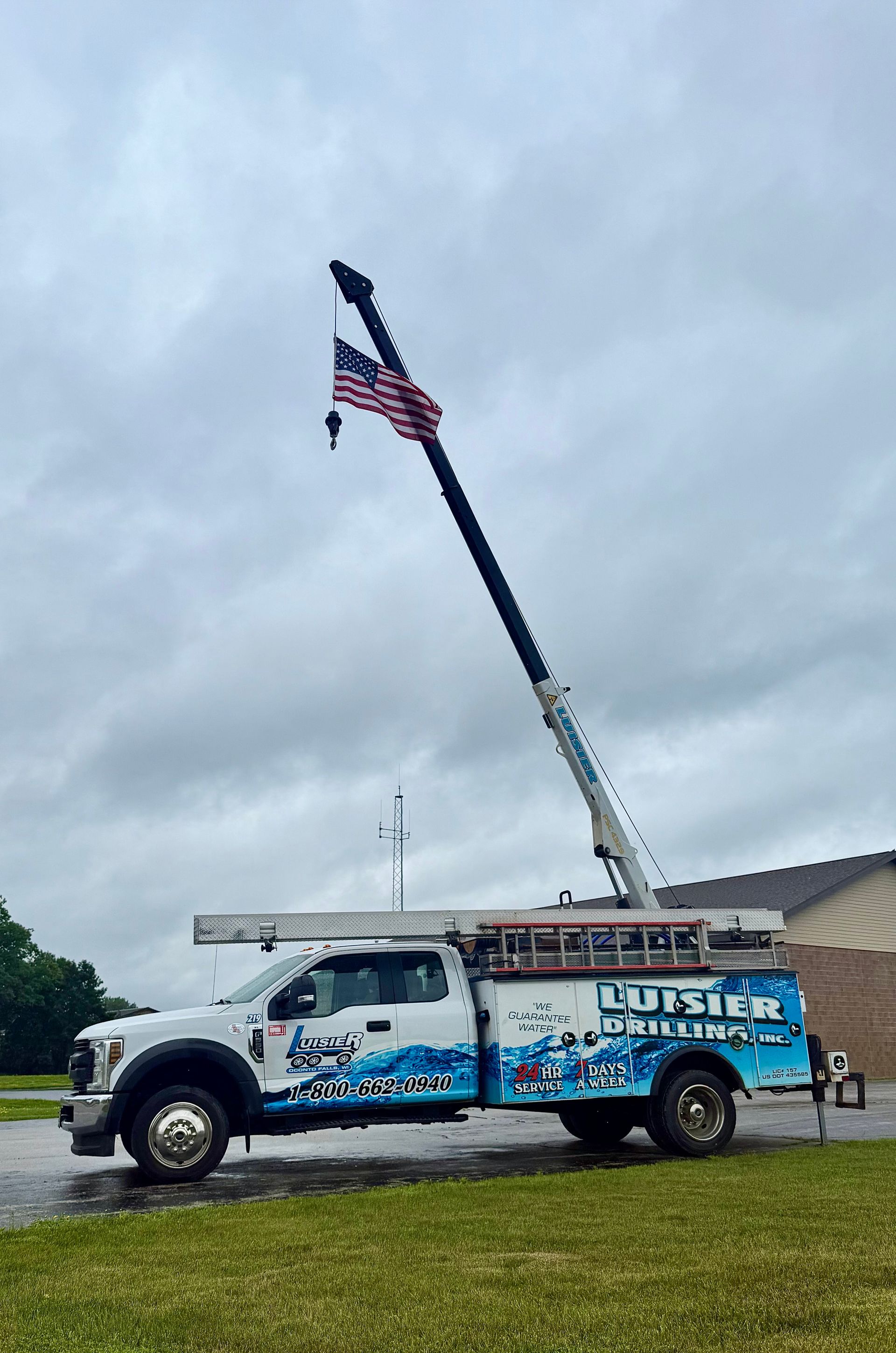 White utility truck with raised crane displaying an American flag under a cloudy sky