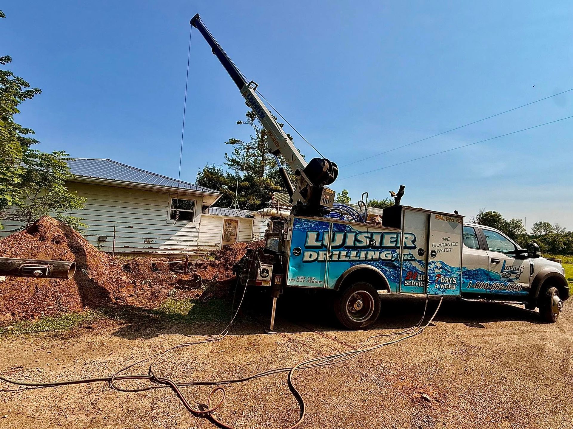 Utility truck with raised crane arm beside a house, likely clearing debris near a brick wall.