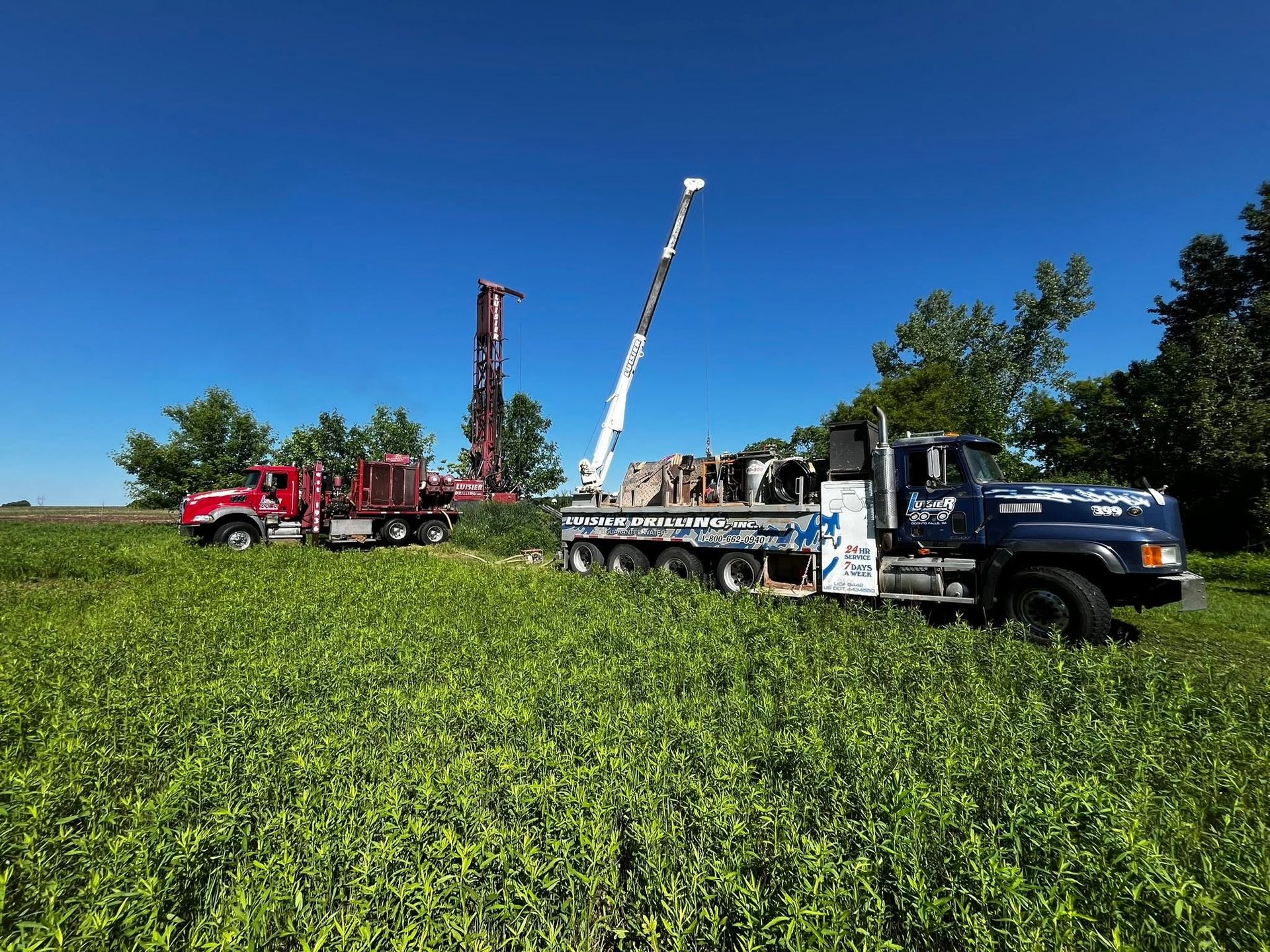 Trucks and a crane in a green field under a clear blue sky