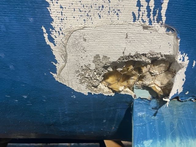 Damaged blue object with a section missing, revealing a porous interior. White and yellow materials are visible.