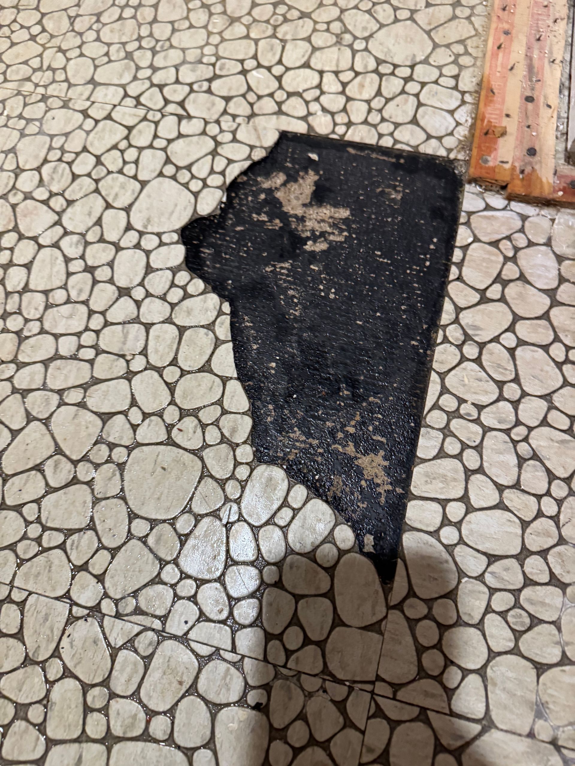 Damaged pebble-stone tile floor with a large black patch in the center, and a small area of a different tile in the upper right.