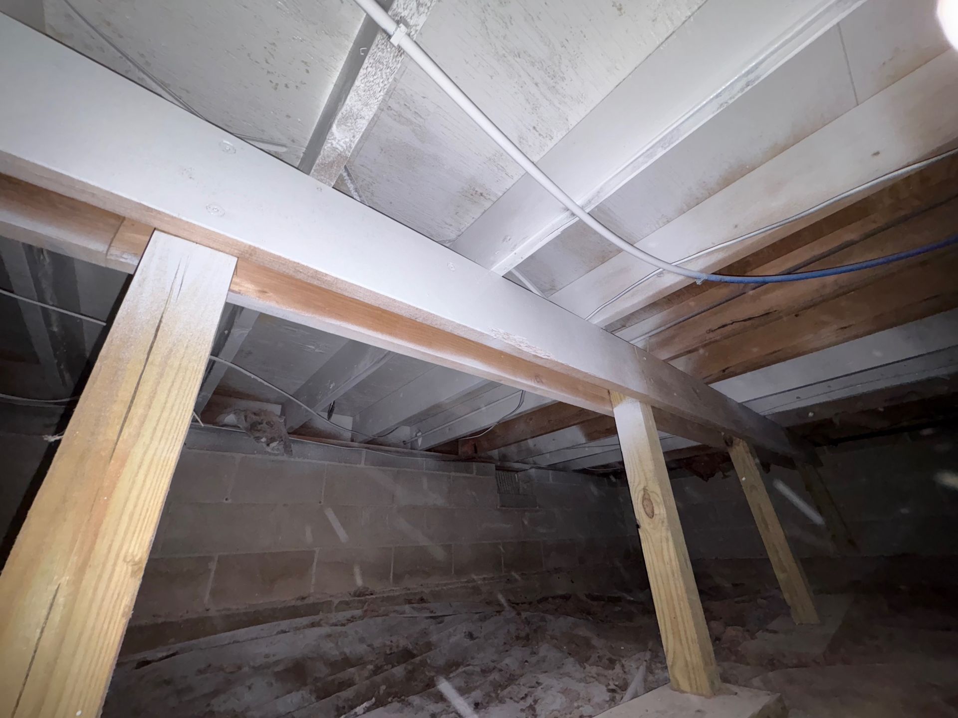 View of a crawl space with support beams, wood, and concrete foundation.