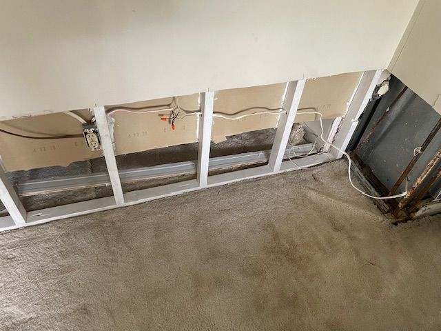 Wall with exposed wooden framing, electrical wires, and damaged drywall.