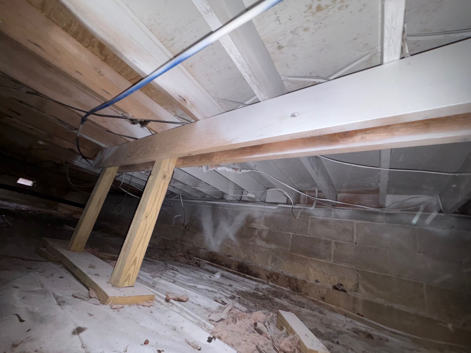 Attic view: Wooden beams and supports, electrical wiring, and cinder block walls are visible.