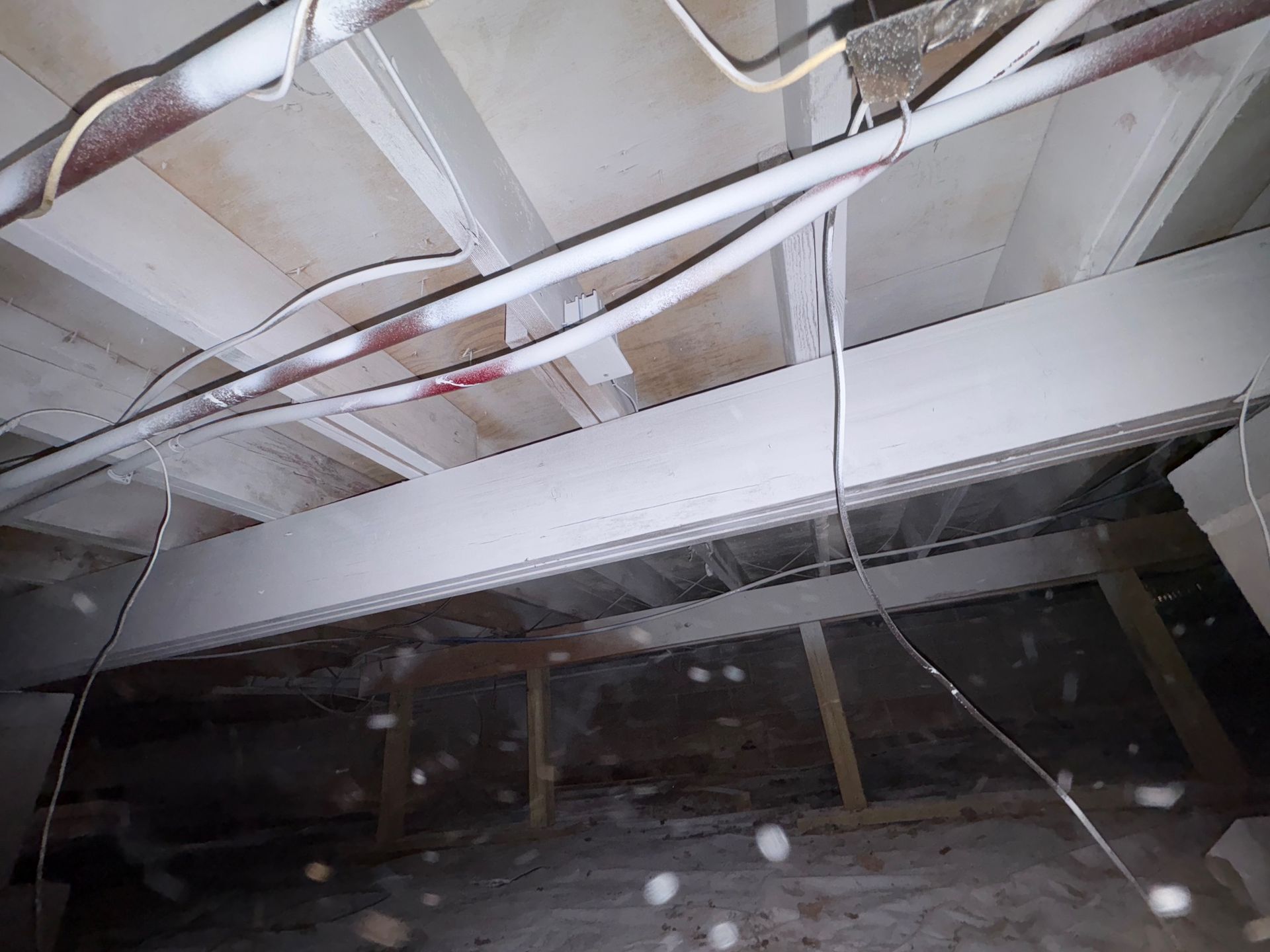 View of a crawl space ceiling with insulation, electrical wiring, and support beams.