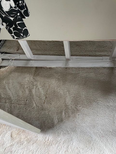 White painted wood under a table sits over a gray carpet with dark shadows.