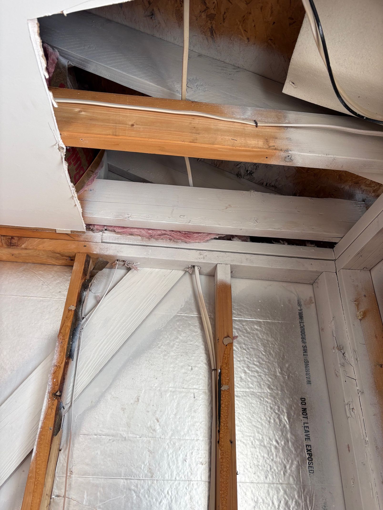 Ceiling and wall framing, partially insulated with foil and white spray foam, partially damaged.