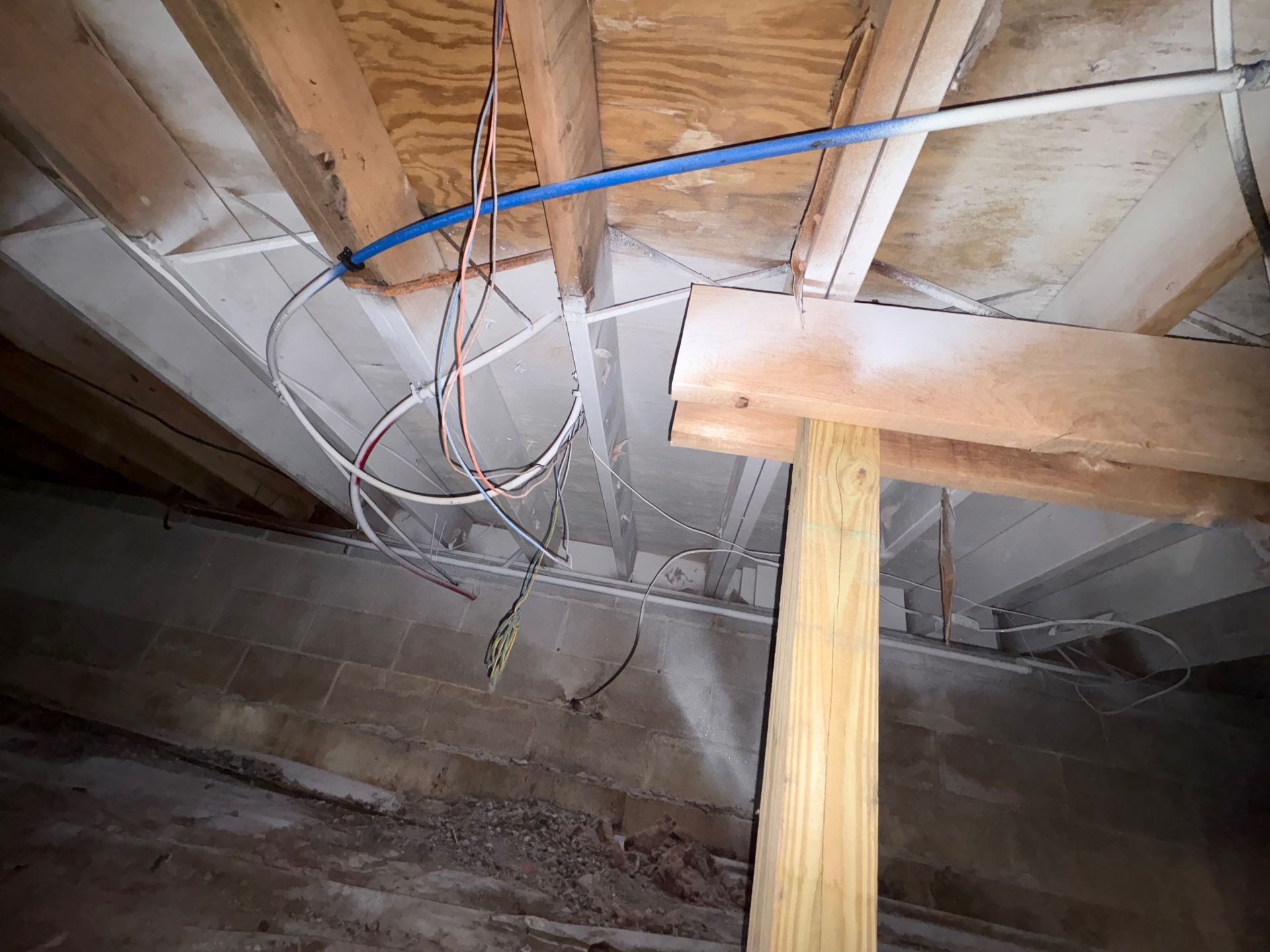 View of an unfinished basement ceiling with exposed wood beams, insulation, and hanging electrical wiring.