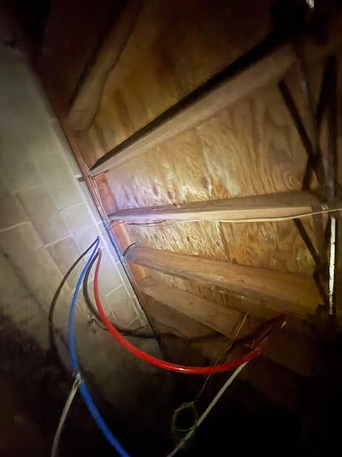 Interior view of an attic space with wooden beams, plywood, and colored water pipes running along a wall.