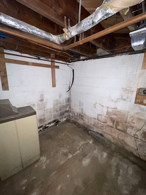 Damp basement corner with a painted white brick wall, visible water damage, and a washing machine.