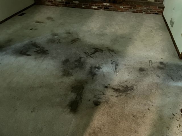 Dirty concrete floor with dark stains and markings, likely in a room near a brick wall.