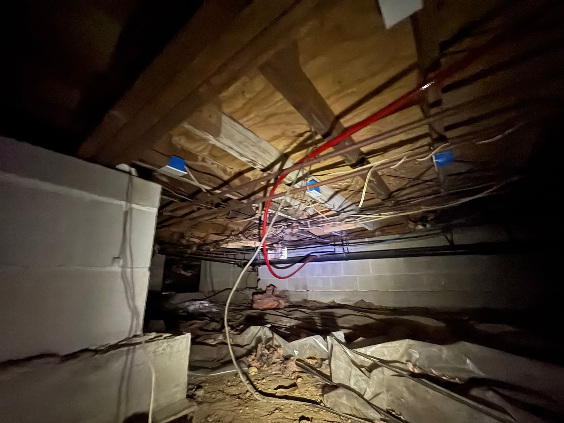 Crawlspace with exposed beams, insulation, and electrical wiring. Interior with block walls and dark shadows.