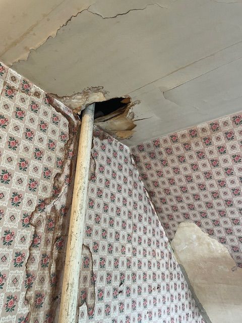 Damaged ceiling with a pipe protruding through a hole, stained floral wallpaper.