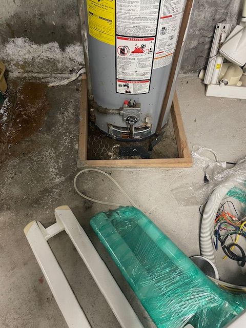 Leaking water heater in basement, surrounded by water stains on the concrete floor.