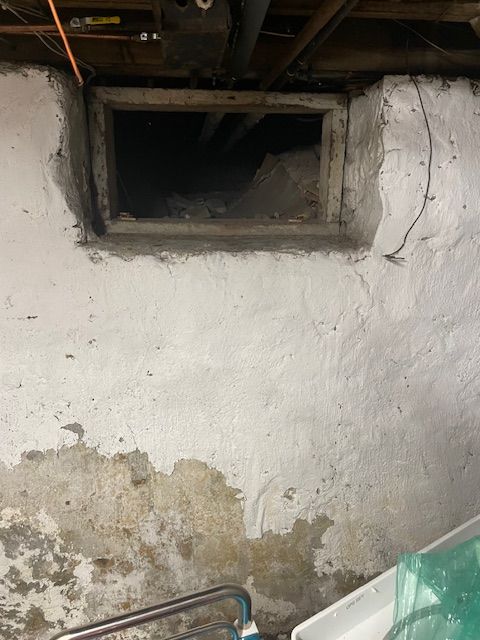 A basement window opening in a white-painted, crumbling concrete wall.