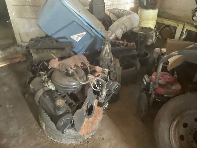 Pile of car engine parts in a cluttered garage, with a blue bin on top.