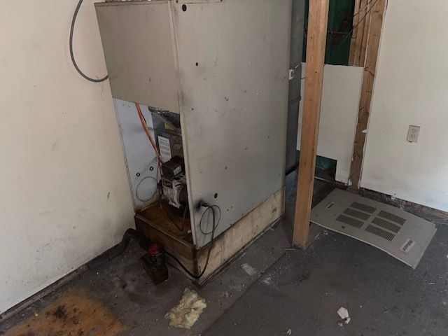 Furnace in a room with water damage; a vent cover is on the floor.