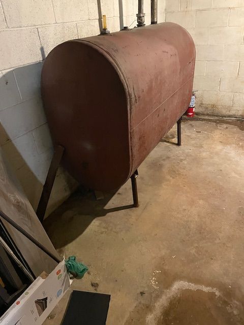 Red oil tank in a basement, supported by a metal frame, against a concrete wall.