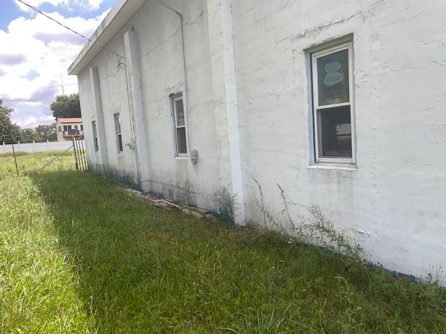 White building with several windows, overgrown grass. Sunny day.
