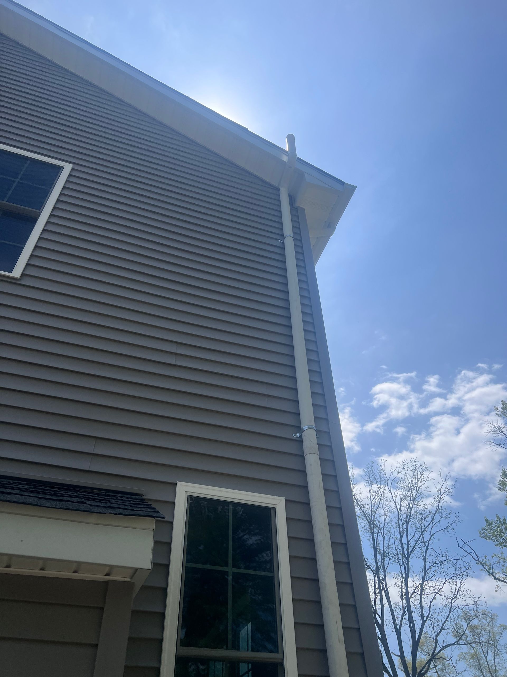 Gray house exterior with siding, a window, and a white gutter against a blue sky.