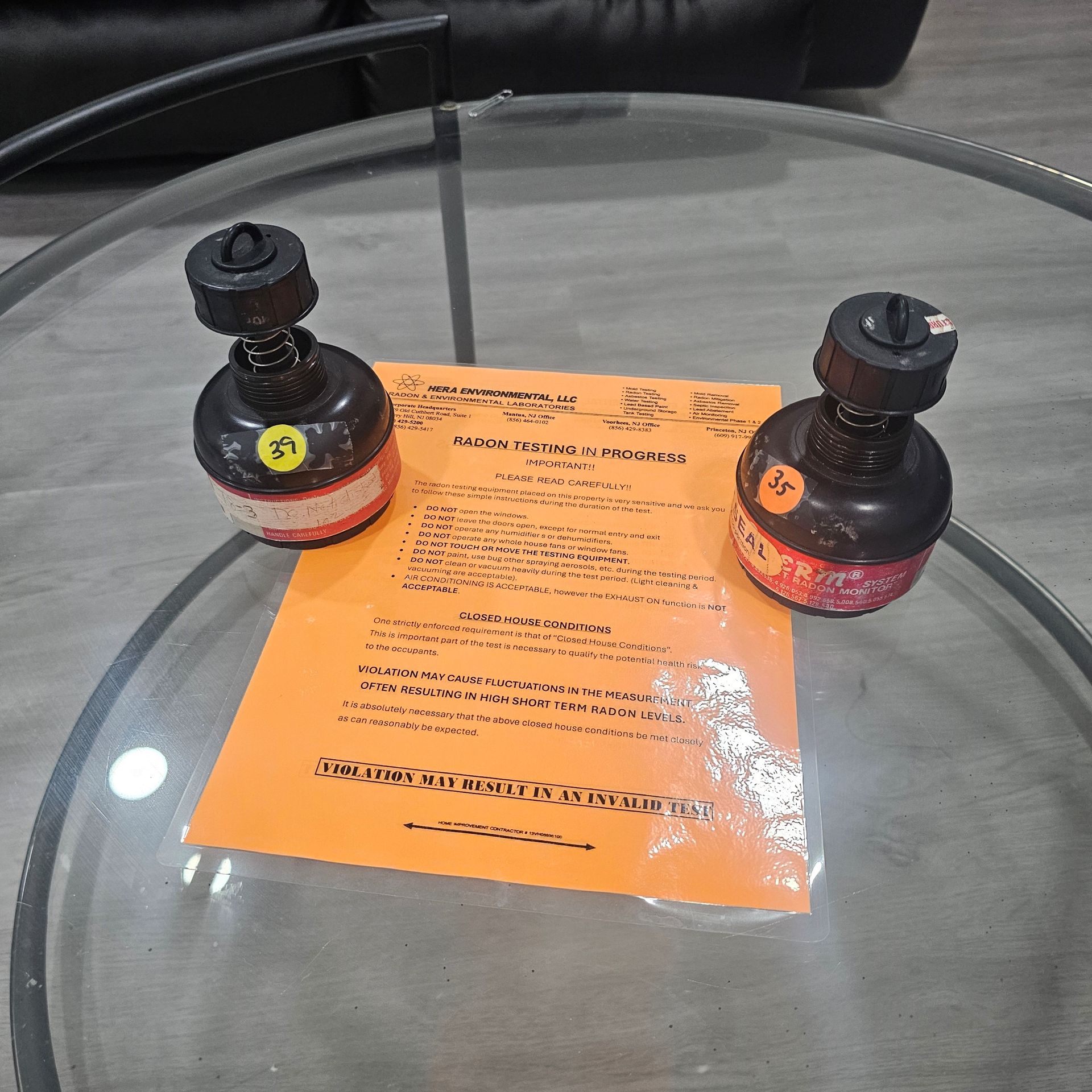 Two black devices with red bands and orange stickers sit on a glass table next to an orange paper.
