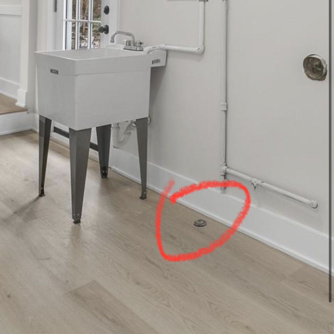Laundry room. White utility sink with metal legs. Drain in floor circled in red.