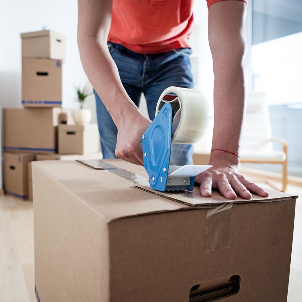 Man taping cardboard box for moving. Boxes stacked, room setting.