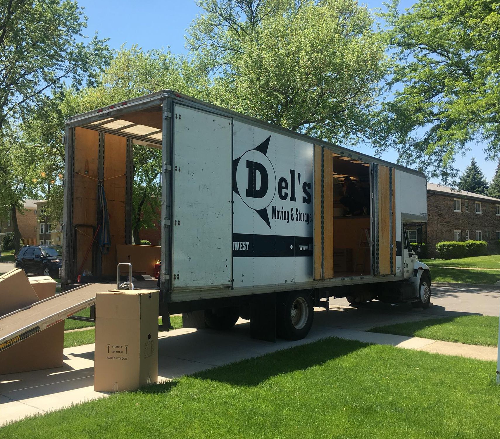 Moving truck with ramp parked in front of a house, boxes and belongings being loaded, sunny day.