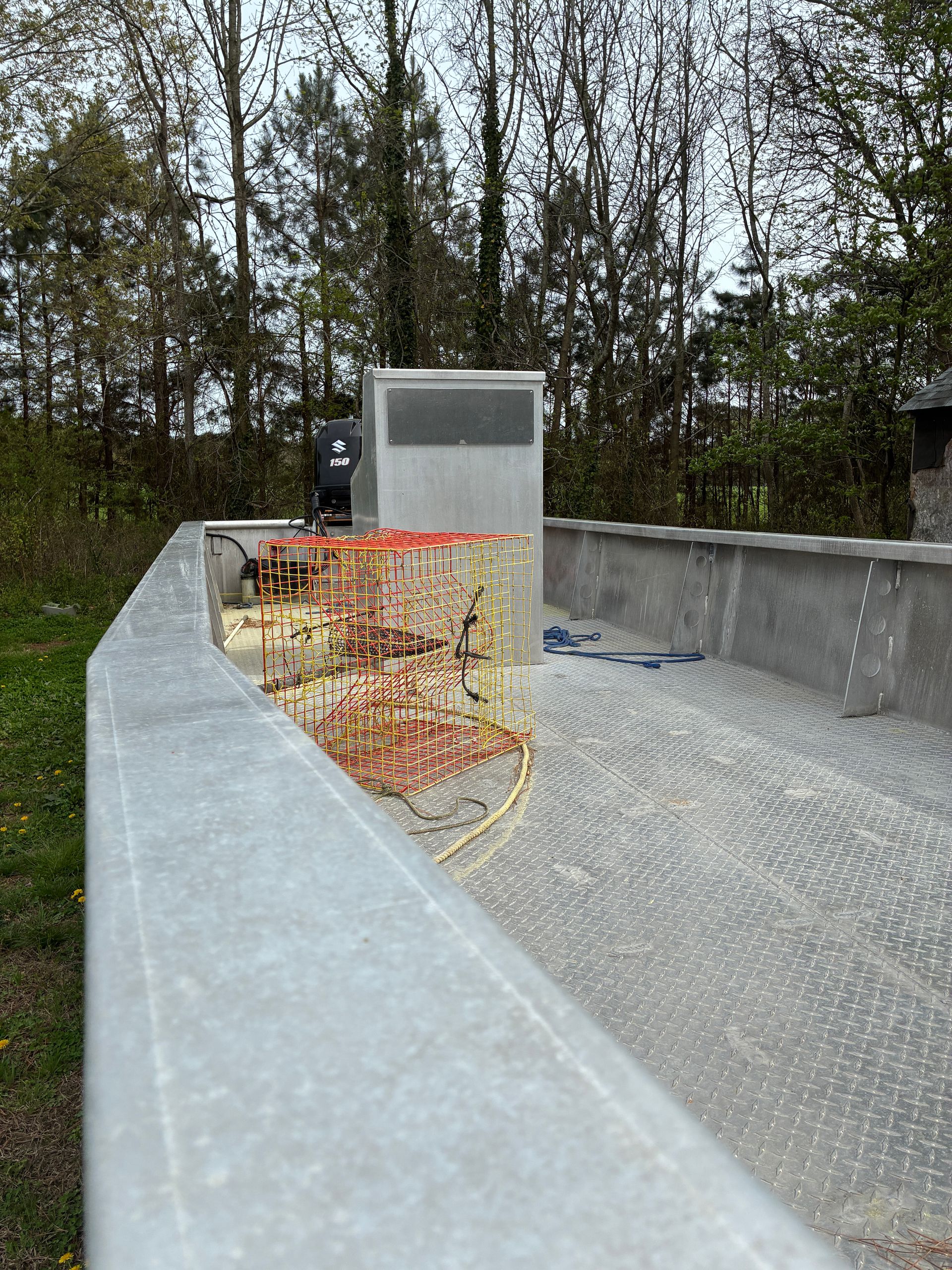 A grave site featuring a metal monument and a wreath of red and yellow flowers set against a backdrop of trees.