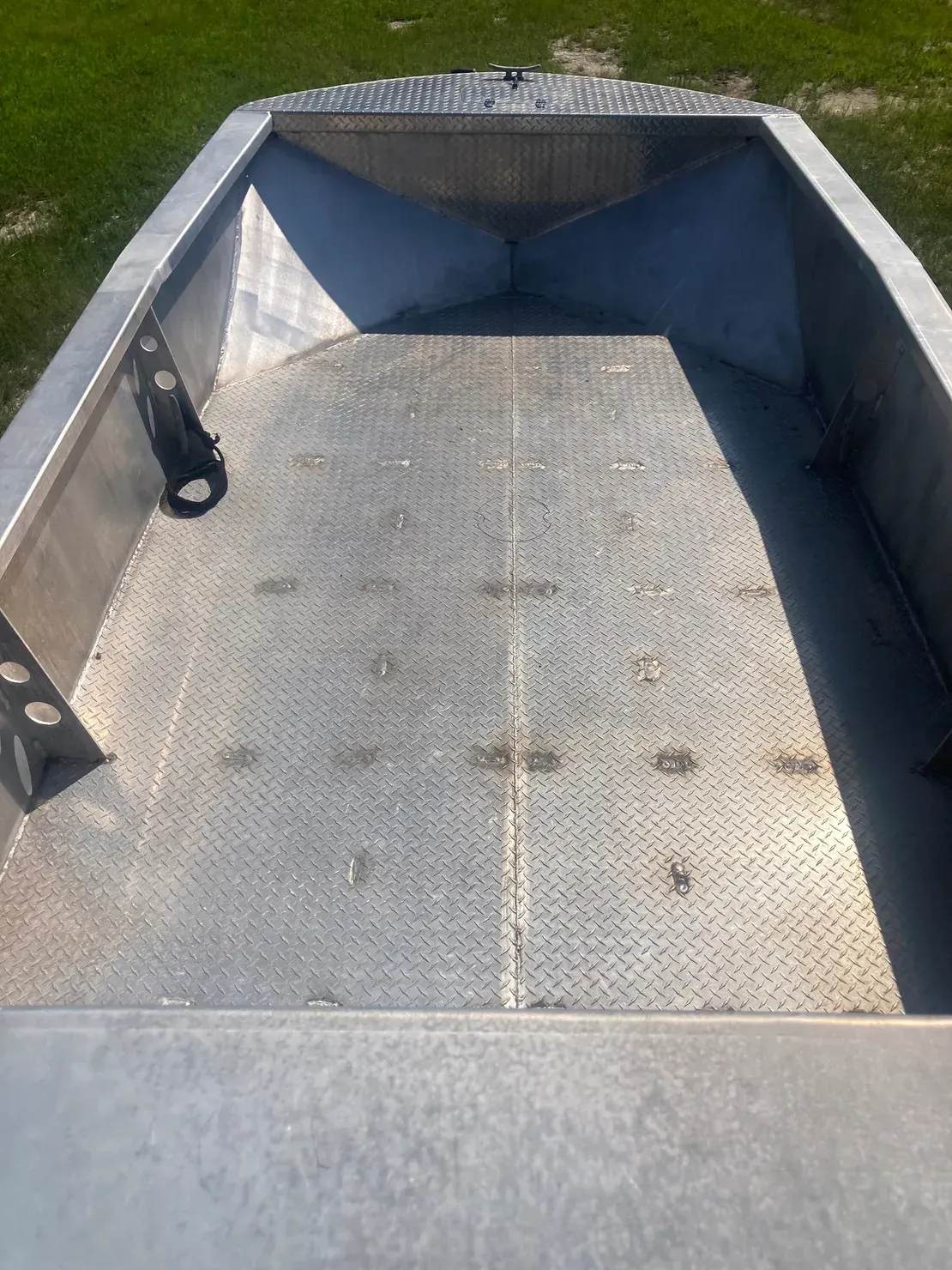 An empty aluminum boat interior featuring a diamond-plate metal floor and front bow deck.